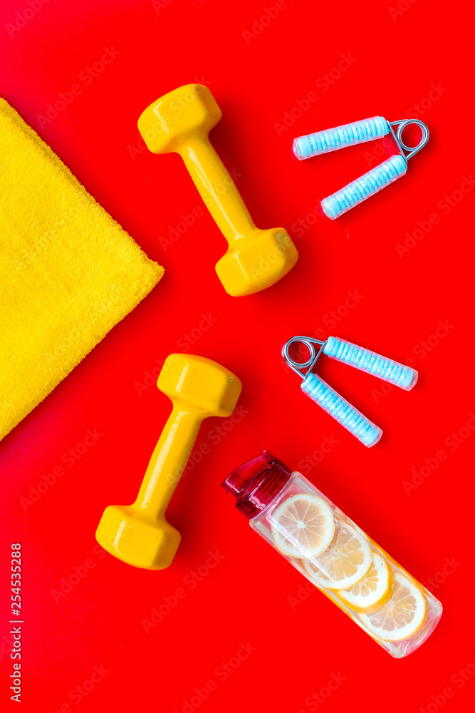 Fitness set with bars, towel, bottle of water and wrist builder on red background top view Fitness set with bars, towel, bottle of water and wrist builder on red background top view