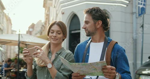 Caucasina happy couple having sightseeing in the city - man reading a map and woman taking photos with a photocamera. photo