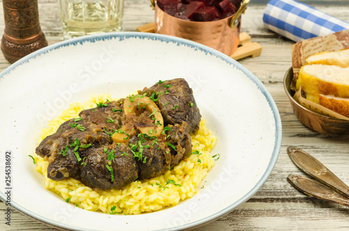 Beef osso bucco with risotto on rustic background. 