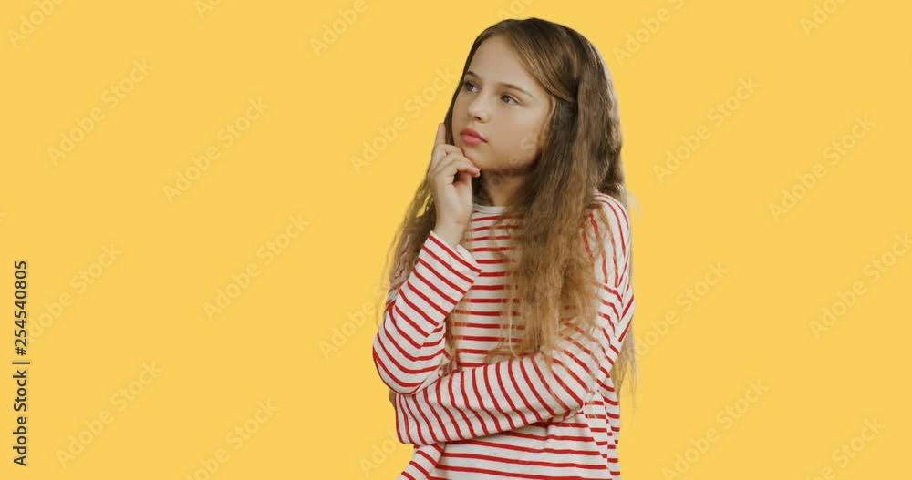 Portrait shot of the cute schoolgirl with long hair standing on the yellow wall background and thinking. Portrait shot of the cute schoolgirl with long hair standing on the yellow wall background and thinking.