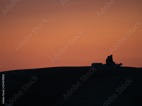 Tokyo Japan-March 11  2019  A silhouette of two persons sit on a bench with a dog on a hill at sunset