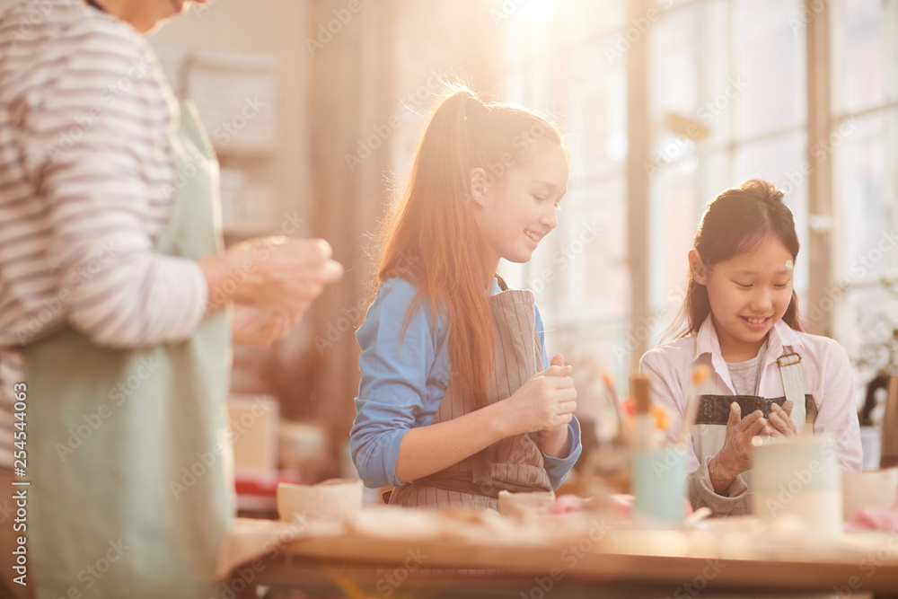 Multi-ethnic group of children creating handmade pottery in art class lit by sunlight, copy space Multi-ethnic group of children creating handmade pottery in art class lit by sunlight, copy space