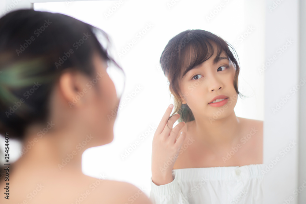 Beauty portrait young asian woman smiling look at mirror of checking skin care caucasian with wellness in the bedroom, beautiful girl happy touching face in reflection for health, lifestyle concept. Beauty portrait young asian woman smiling look at mirror of checking skin care caucasian with wellness in the bedroom, beautiful girl happy touching face in reflection for health, lifestyle concept.