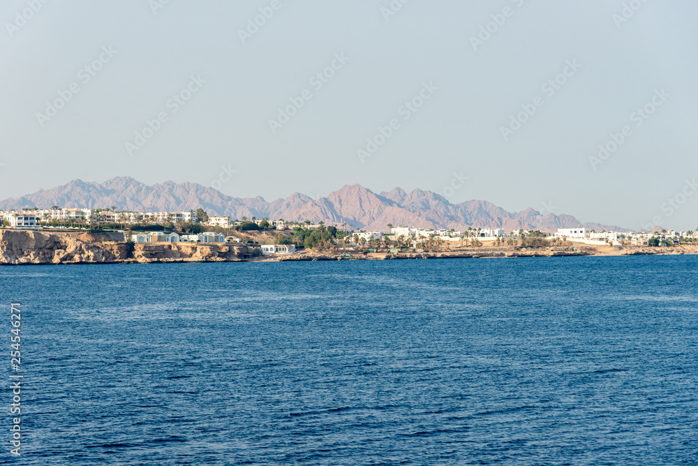 hotels and houses in the distance stand over a cliff above the blue sea hotels and houses in the distance stand over a cliff above the blue sea