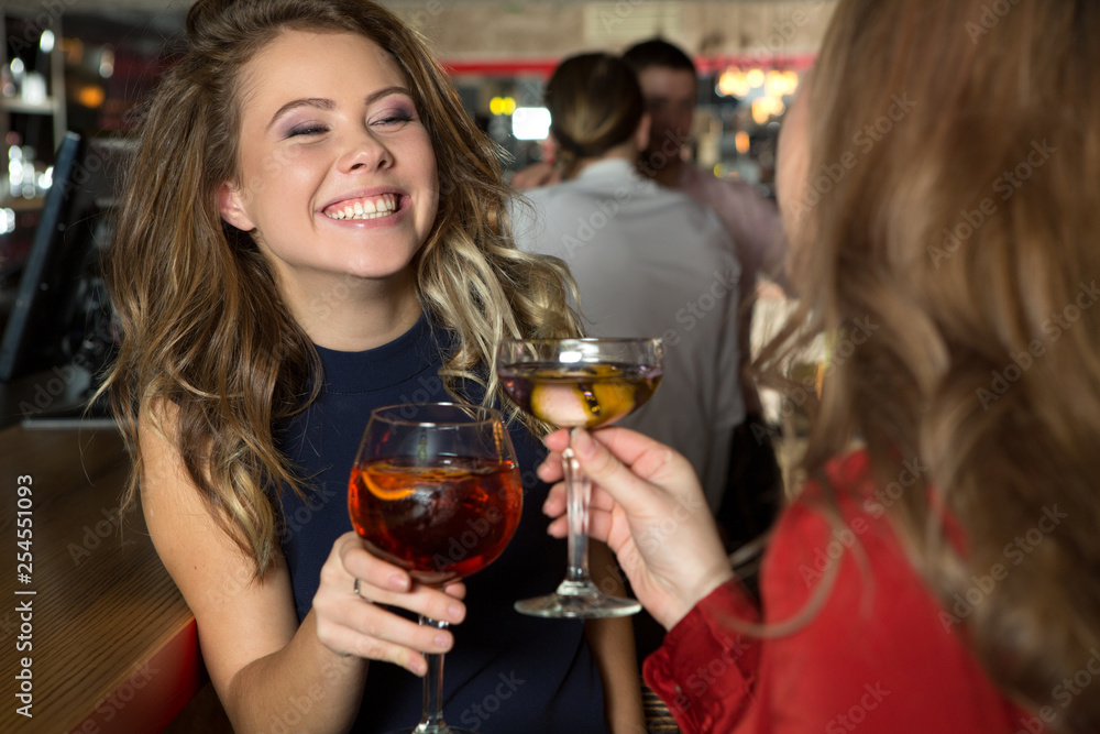 Sharing happy moments. Beautiful female showing her perfect smile and listening to her friendat the bar.