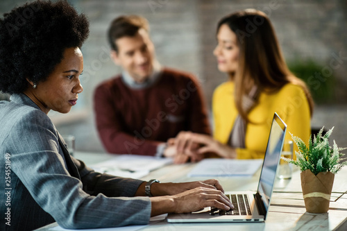 Black female insurance agent working on computer during a meeting with her clients.