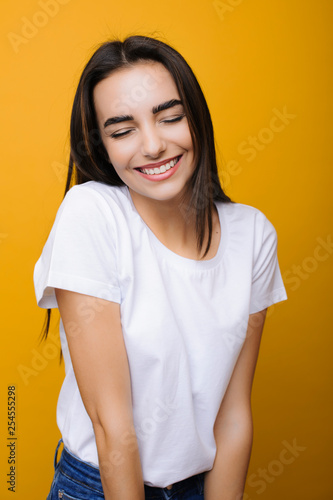 Portrait of a lovely attractive girl being happy with closed eyes laughing isolated on a yellow background.