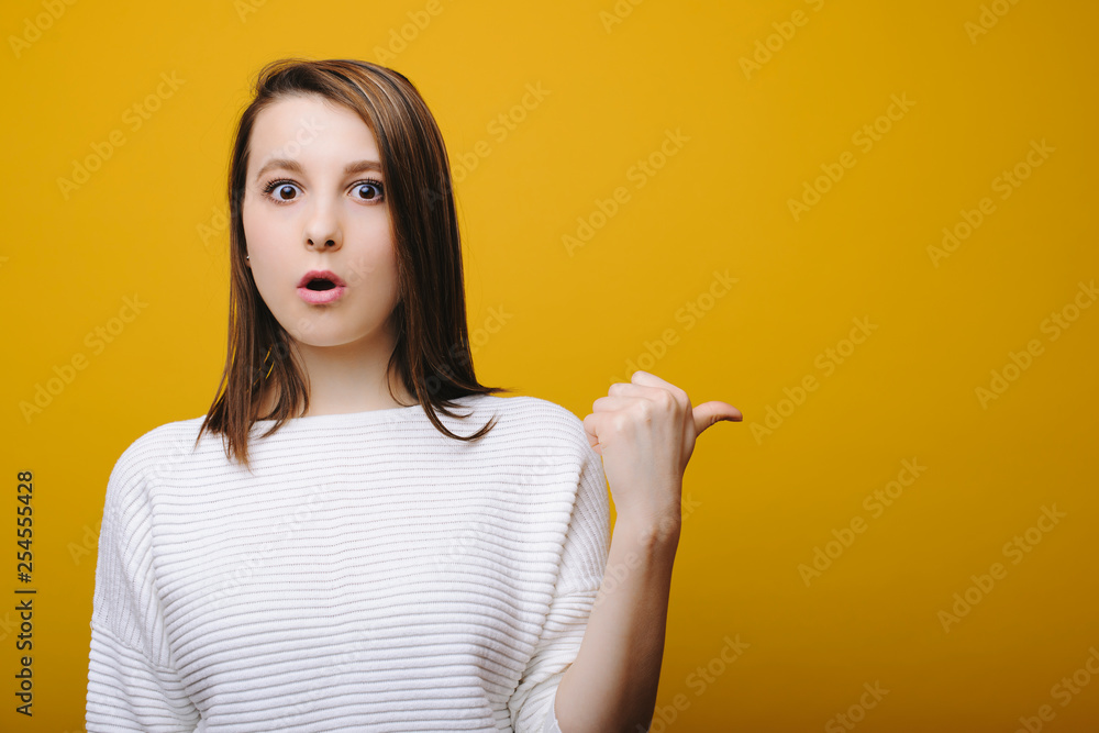 Beautiful young european girl looking at camera amazed and showing away isolated on yellow background. Beautiful young european girl looking at camera amazed and showing away isolated on yellow background.