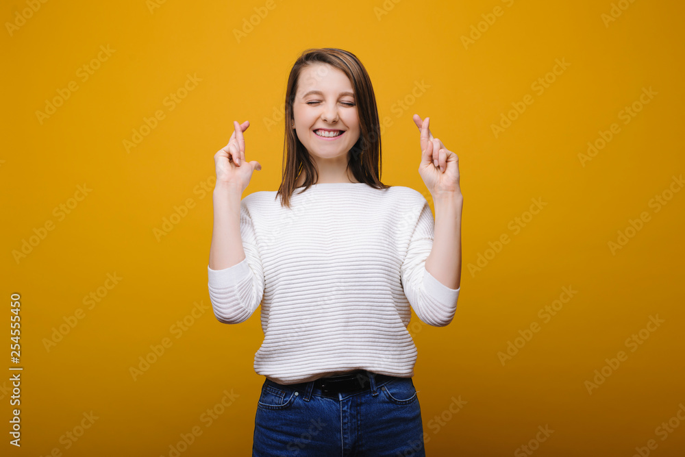 Isolated young lovely female with closed eyes and crossed fingers on both hands thinking about to win in front of a yellow background. I want to win concept. Isolated young lovely female with closed eyes and crossed fingers on both hands thinking about to win in front of a yellow background. I want to win concept.