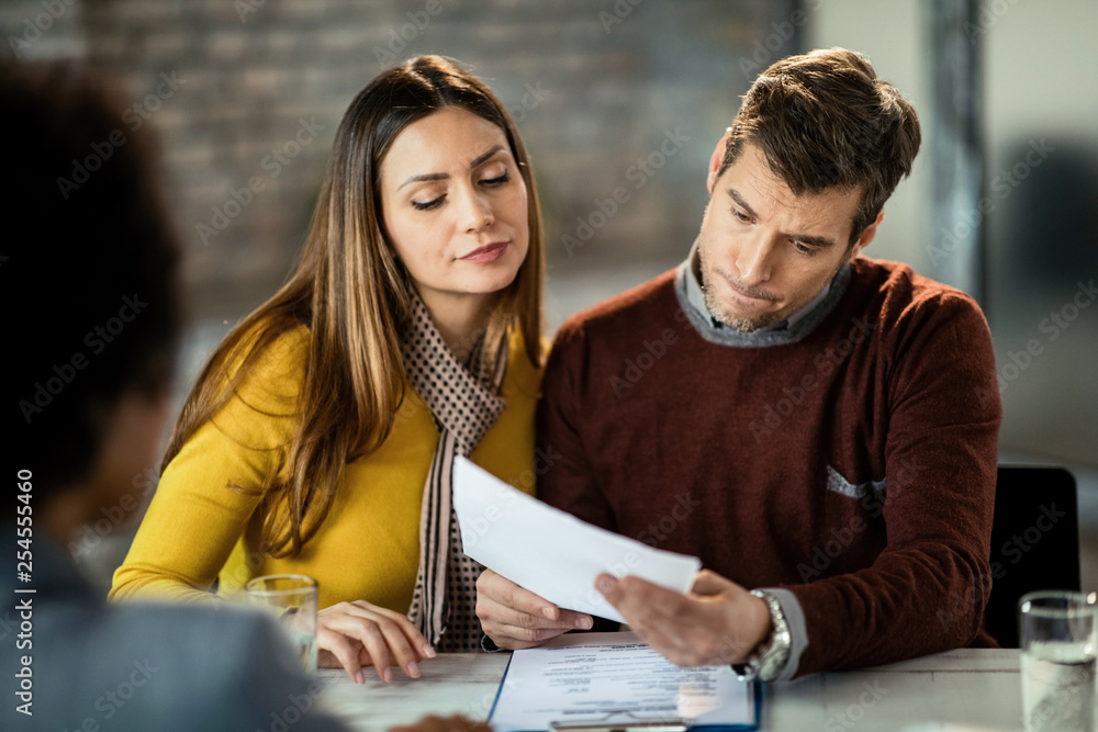 Couple having doubts while reading financial reports on a meeting with insurance agent. Couple having doubts while reading financial reports on a meeting with insurance agent.