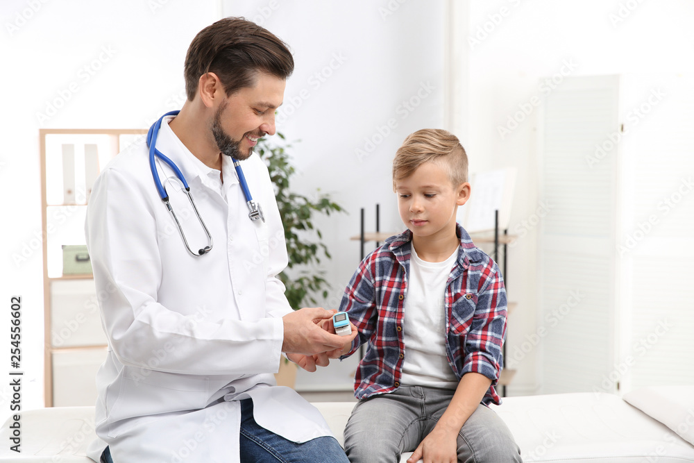 Doctor checking little boy's pulse with medical device in hospital Doctor checking little boy's pulse with medical device in hospital