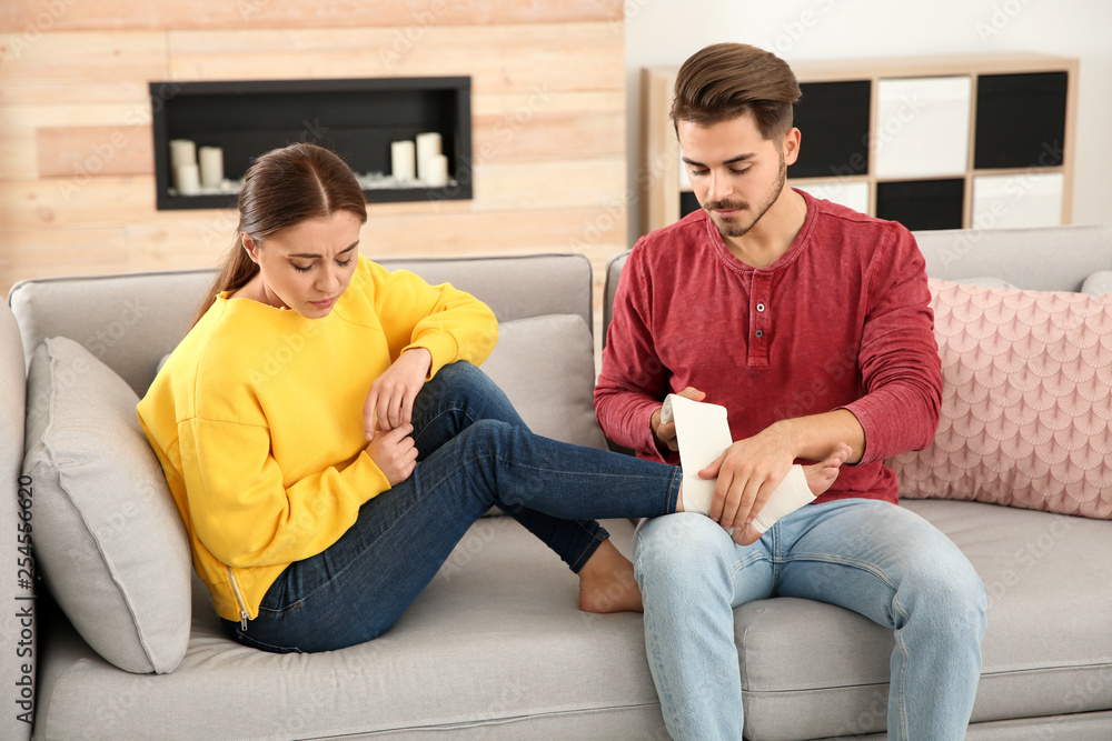 Young man applying bandage on woman's injured leg at home. First aid Young man applying bandage on woman's injured leg at home. First aid