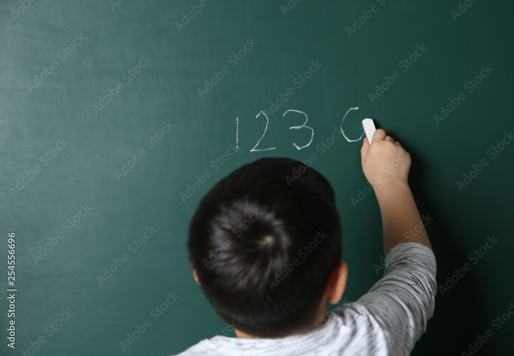 Child writing math sum on chalkboard. Space for text