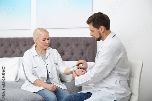 Doctor checking mature woman's pulse with medical device in bedroom