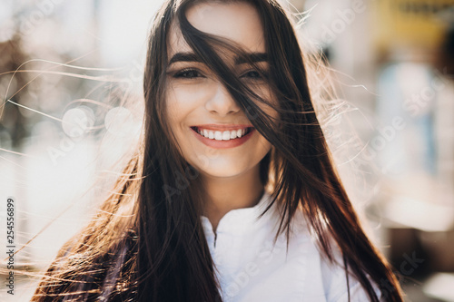 Close up portrait of a amazing long haired girl looking at camera laughing while the wind blows her hair outside on the street. Happy woman concept. photo