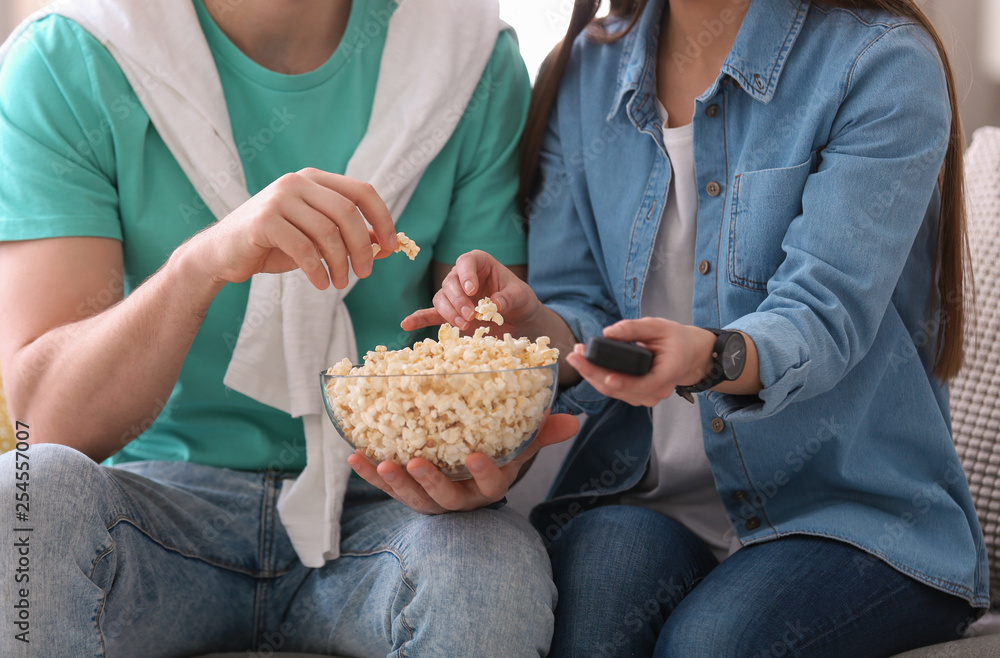 Couple watching movie with popcorn at home, closeup
