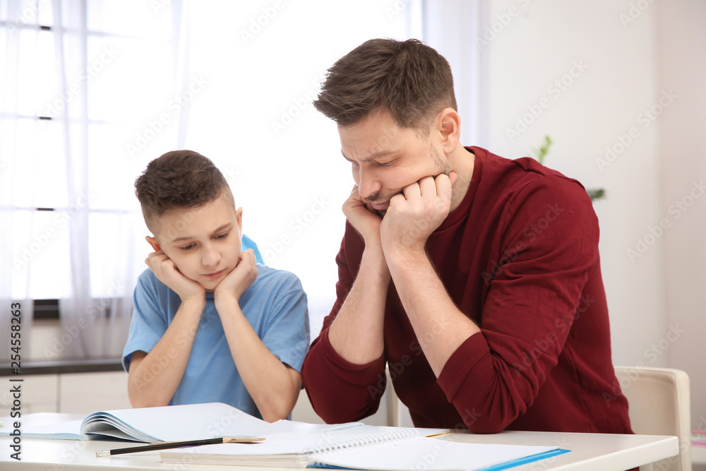 Dad helping his son with difficult homework assignment in room Dad helping his son with difficult homework assignment in room