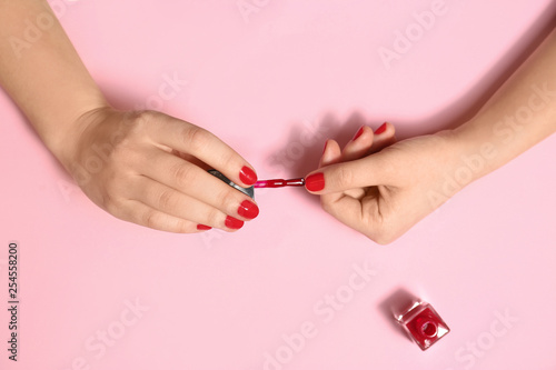 Woman applying nail polish on color background  top view