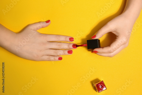 Woman applying nail polish on color background, top view