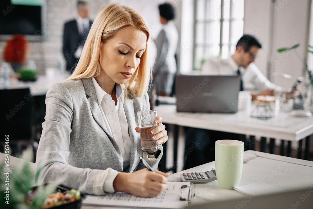 Businesswoman witting notes while going through business reports at work. Businesswoman witting notes while going through business reports at work.