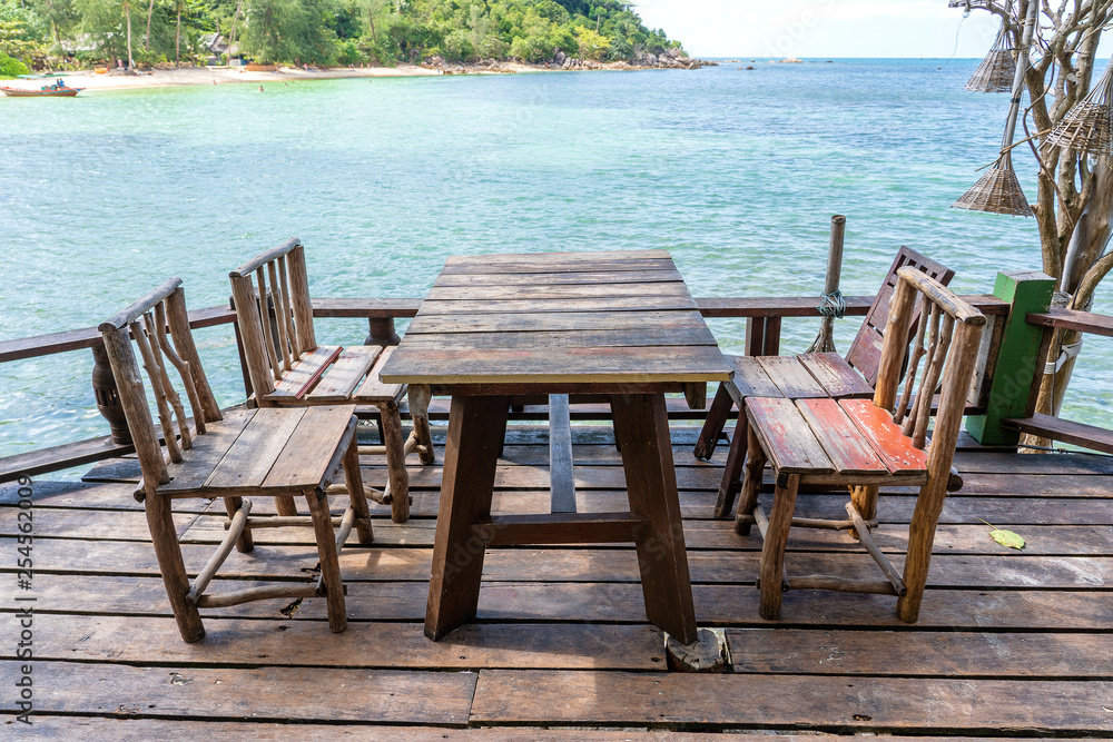 Wooden table and chairs in empty beach cafe next to sea water. Island Koh Phangan, Thailand Wooden table and chairs in empty beach cafe next to sea water. Island Koh Phangan, Thailand