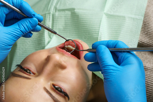 Dentist examines teeth of woman. Young girl with open mouth. White teeth. Dentist hands with medical instruments. Close-up. Dental clinic.