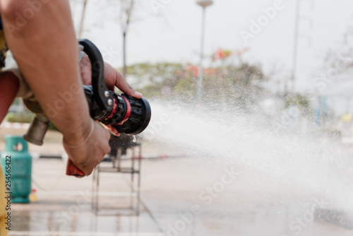Firefighter hand holding water hose and water spraying from red fire truck.Rescue man fighting training.Fire man spray high pressure water to fire and copy space.Selective focus