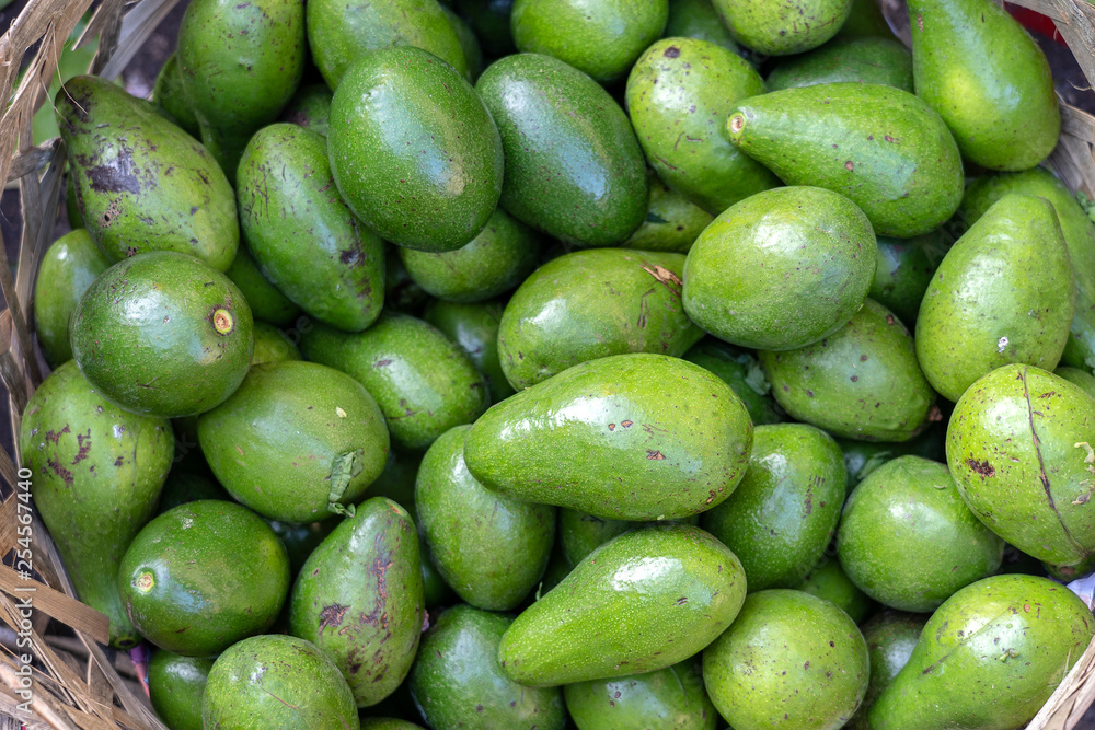 Green avocado on the bamboo or wooden basket in traditional street market in Ubud, Bali, Indonesia , closeup Green avocado on the bamboo or wooden basket in traditional street market in Ubud, Bali, Indonesia , closeup