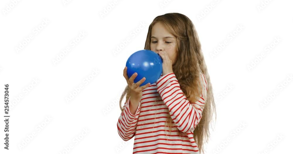 Cute blond teenage little girl with a long hair inflating a blue balloon on the white wall background. Cute blond teenage little girl with a long hair inflating a blue balloon on the white wall background.