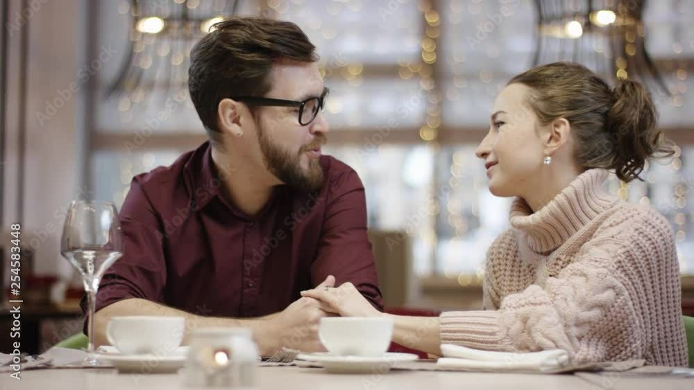 Pretty couple are flirting with each other by table in restaurant holding each others hand Pretty couple are flirting with each other by table in restaurant holding each others hand