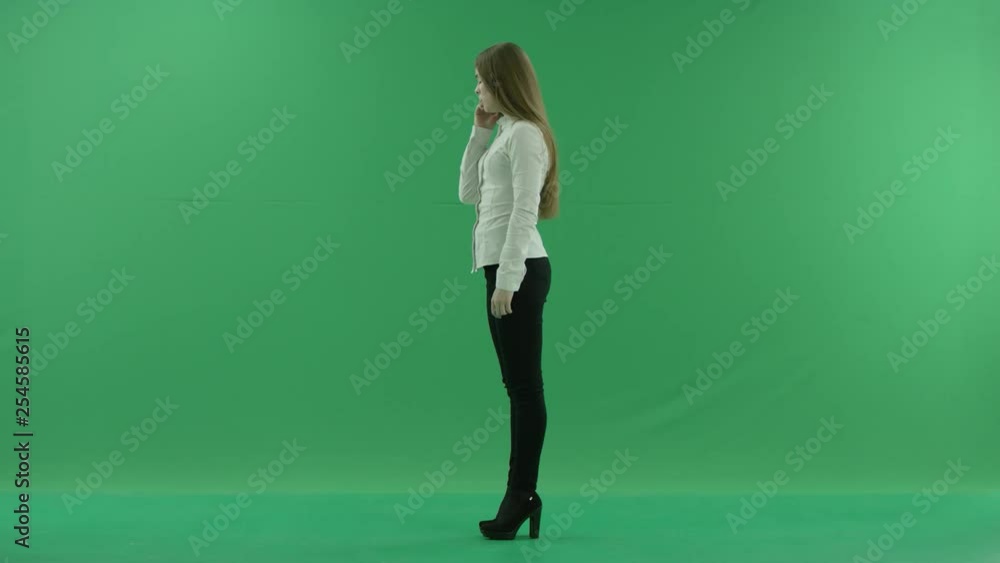 Annoyed young business woman is talking on mobile phone standing fullength sideways in the centre of a Green Screen Annoyed young business woman is talking on mobile phone standing fullength sideways in the centre of a Green Screen
