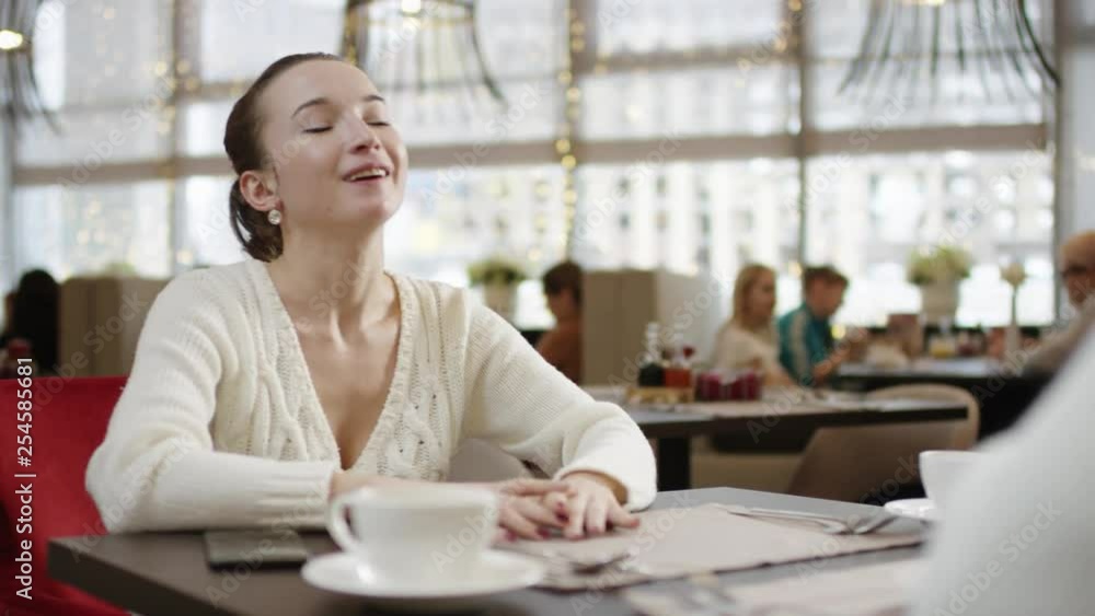 Young woman laughing while chatting with her friend in a restaurant Young woman laughing while chatting with her friend in a restaurant