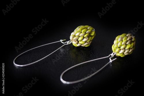 Beaded earrings green color made of superduo beads on a dark background close up photo