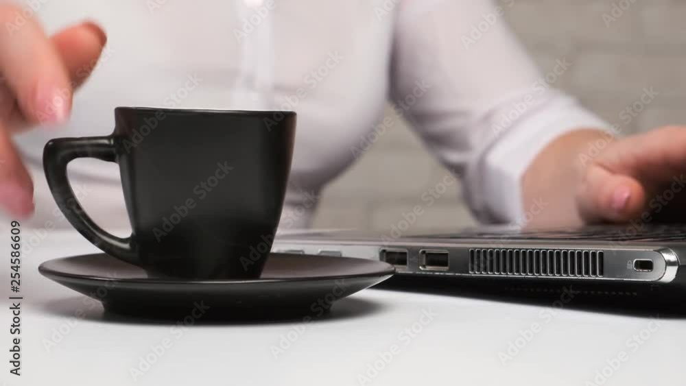 woman drinks hot coffee and works on computer in office. woman drinks hot coffee and works on computer in office.