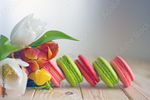 French macarones red, pink and green on a wooden background next to spring flowers. Sweet dessert from France, colorful cookies made from almond flour and egg whites.Confectionery background photo