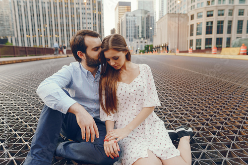 beautiful long-haired girl in summer dress with her handsome husband in white shirt and pants sitting in sunny Chicago