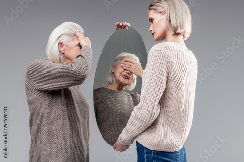 Impressed old lady closing her eyes while looking in mirror