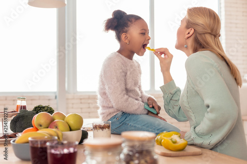 Blonde-haired mother feeding her cute funny girl with fruits