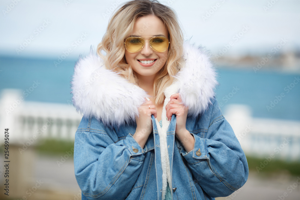 The girl enjoying the warm autumn day.Portrait of beautiful girl near the water.Portrait of a beautiful woman in a blue jacket outdoors in early spring on the ocean coast.Spring portrait on the beach. The girl enjoying the warm autumn day.Portrait of beautiful girl near the water.Portrait of a beautiful woman in a blue jacket outdoors in early spring on the ocean coast.Spring portrait on the beach.