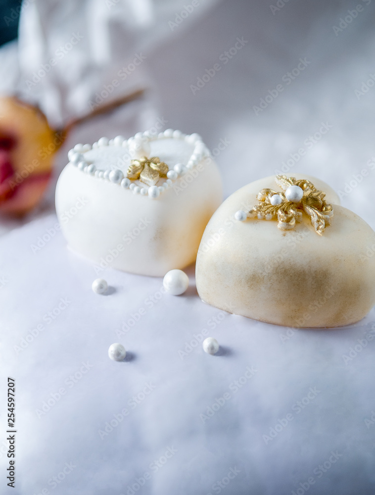 Sponge cake covered with a mirror glaze. Decorated with two white chocolate hearts. On a white background next to the cake are three orange roses. Dark photo. Copy space. Place for text Sponge cake covered with a mirror glaze. Decorated with two white chocolate hearts. On a white background next to the cake are three orange roses. Dark photo. Copy space. Place for text
