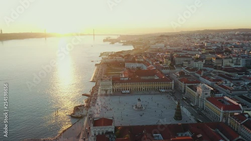 Aerial view; drone flight over the Lisbon cityscape; panorama of Portuguese capital with main Commerce Square, Tagus river; last sunbeams shining and illuminated ginger rooftops; touristic places