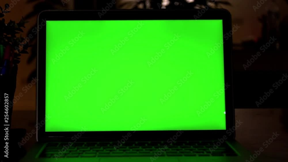 Laptop Computer Showing Green Chroma Key Screen Stands on a Desk in the Living Room. In the Background Cozy Living Room in the Evening with Warm Lights on. Zoom out Shot. 4K Laptop Computer Showing Green Chroma Key Screen Stands on a Desk in the Living Room. In the Background Cozy Living Room in the Evening with Warm Lights on. Zoom out Shot. 4K