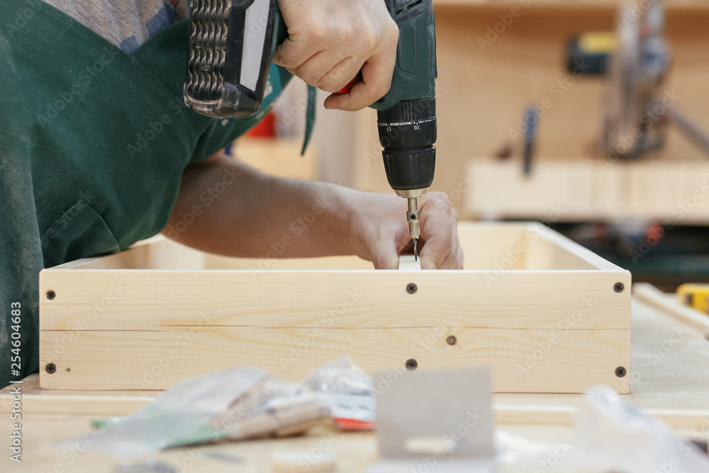 Experienced worker in a carpentry workshop creates a wooden product with raw boards and connects them with screws with a screwdriver. Concept of woodwork in carpentry Experienced worker in a carpentry workshop creates a wooden product with raw boards and connects them with screws with a screwdriver. Concept of woodwork in carpentry