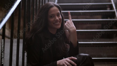 Medium real time shot of an attractive woman gesturing one with one finger while sitting outdoors