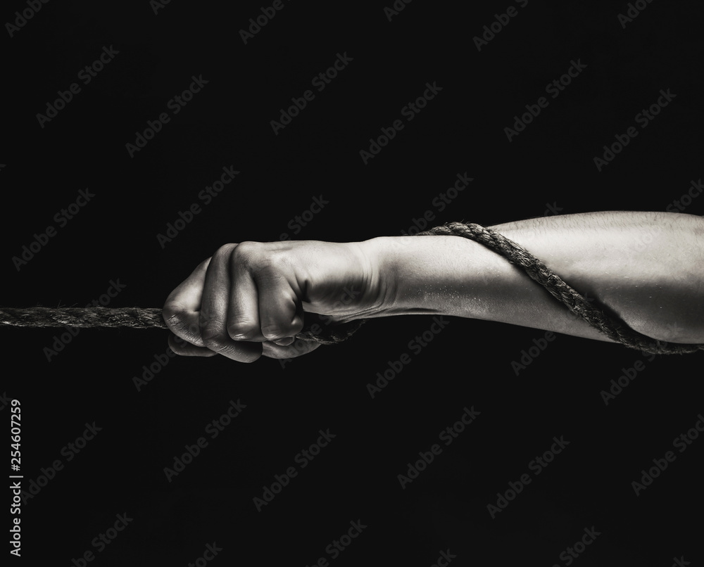 Man's hand holding on to the rope. Hand holding a rope, climbing rope,  strength and determination concept. Rope, cord. Safety. Macro shot isolated  over black background. Black and white. Stock Photo