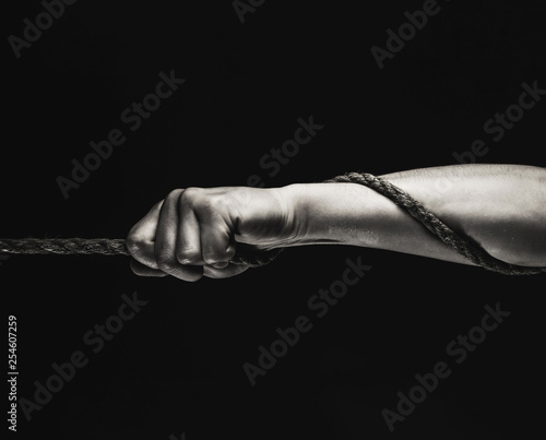 Man's hand holding on to the rope. Hand holding a rope, climbing rope, strength and determination concept. Rope, cord. Safety. Macro shot isolated over black background. Black and white.