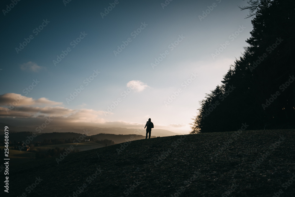 a man with backpack standing on a hill in europe in the afternoon at sunset