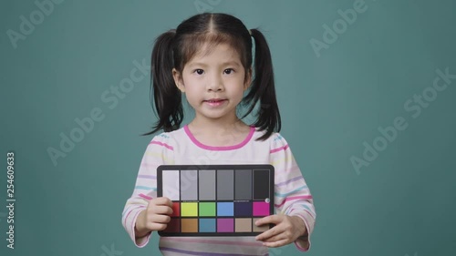 Portrait of little asian girl holding the Color Checker Chart on the green background, For Photography or Videography