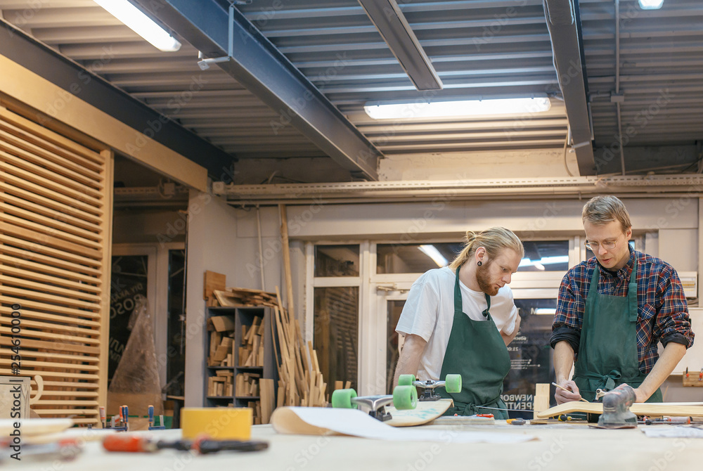 Two male carpenters a teacher and a student are working on a new product in their carpentry workshop. Concept of creating a new wooden handmade goods Two male carpenters a teacher and a student are working on a new product in their carpentry workshop. Concept of creating a new wooden handmade goods