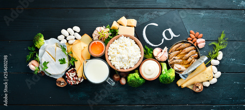 Products containing natural calcium: cheese, milk, parmesan, sour cream, fish, almonds, parsley, garlic, broccoli. On a black wooden background. Top view. Free copy space.